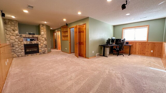 carpeted home office featuring a stone fireplace, a textured ceiling, and wooden walls