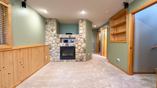 living room with light carpet, a stone fireplace, and wood walls