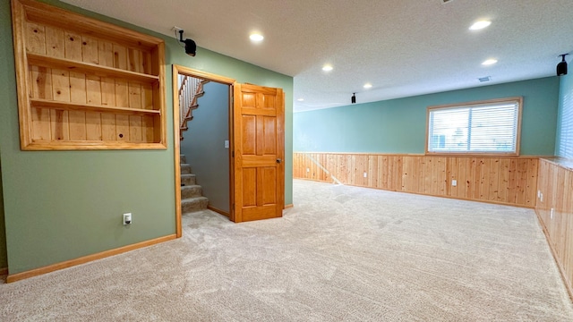 carpeted spare room with wood walls and a textured ceiling