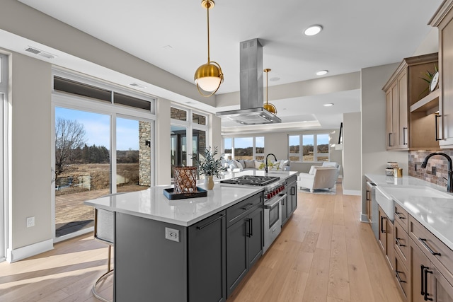 kitchen featuring island range hood, stainless steel gas stovetop, hanging light fixtures, a center island, and light stone countertops