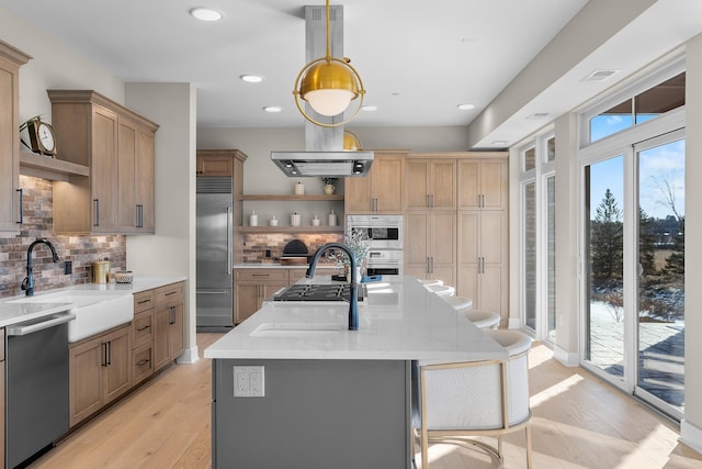 kitchen with stainless steel appliances, light stone countertops, a kitchen island with sink, and sink