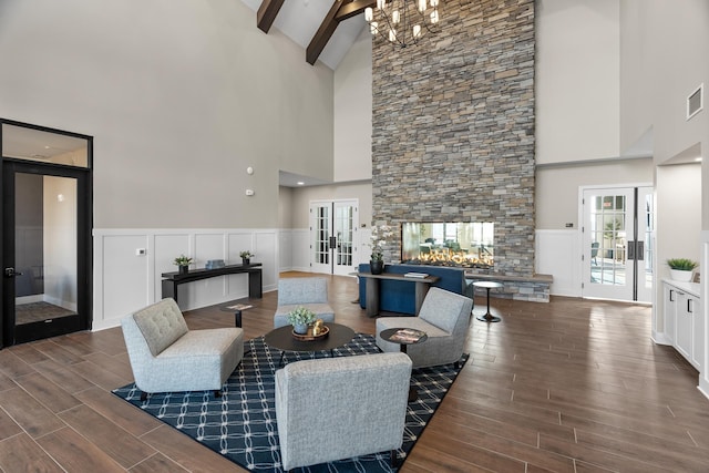 living room featuring lofted ceiling with beams, an inviting chandelier, a fireplace, and french doors