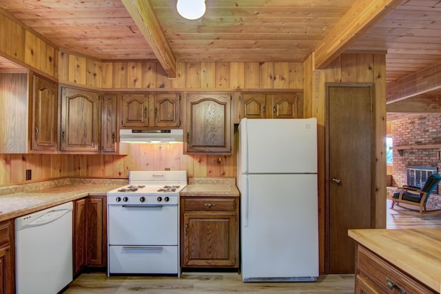 kitchen featuring under cabinet range hood, white appliances, beamed ceiling, and wooden walls
