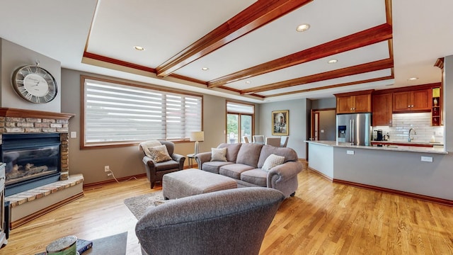 living room featuring beam ceiling, sink, a brick fireplace, and light hardwood / wood-style flooring