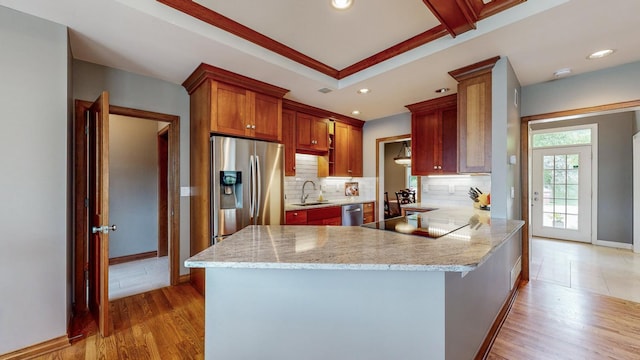 kitchen featuring stainless steel appliances, kitchen peninsula, sink, tasteful backsplash, and light wood-type flooring