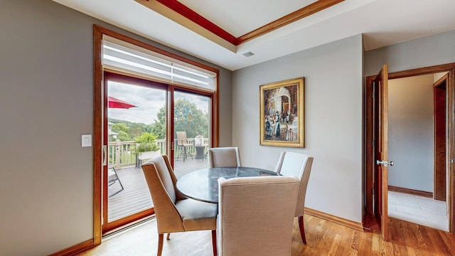 dining space with a raised ceiling, light wood-type flooring, and ornamental molding