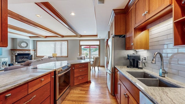 kitchen featuring light stone counters, light wood-type flooring, appliances with stainless steel finishes, sink, and a brick fireplace