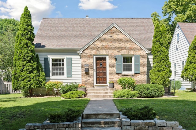 new england style home with stone siding, roof with shingles, and a front yard