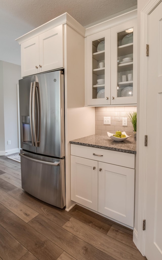 kitchen featuring decorative backsplash, dark hardwood / wood-style flooring, dark stone counters, white cabinets, and stainless steel fridge