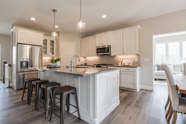 kitchen with a center island with sink, white cabinetry, light hardwood / wood-style flooring, hanging light fixtures, and stainless steel appliances