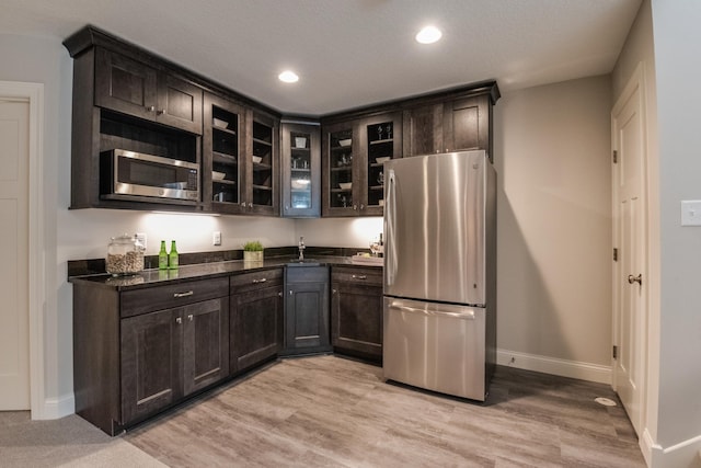 kitchen with appliances with stainless steel finishes, dark stone counters, light hardwood / wood-style floors, sink, and dark brown cabinets