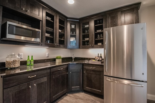 kitchen featuring sink, light hardwood / wood-style flooring, dark brown cabinetry, stainless steel appliances, and dark stone counters