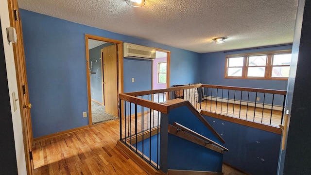 interior space with a textured ceiling, a baseboard heating unit, a wall unit AC, and wood-type flooring