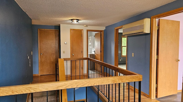 hall with wood-type flooring, a wall unit AC, and a textured ceiling