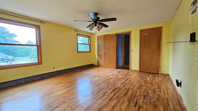 unfurnished bedroom with a baseboard heating unit, multiple windows, a textured ceiling, and hardwood / wood-style flooring