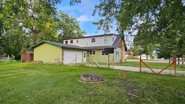 rear view of property featuring an outdoor fire pit, a garage, a lawn, and an outbuilding