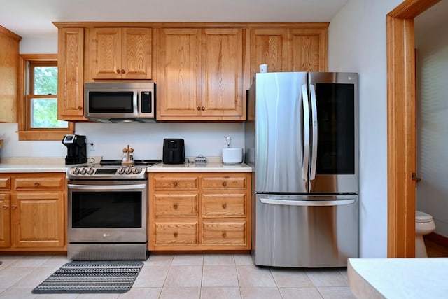 kitchen featuring light tile patterned floors, stainless steel appliances, brown cabinets, and light countertops