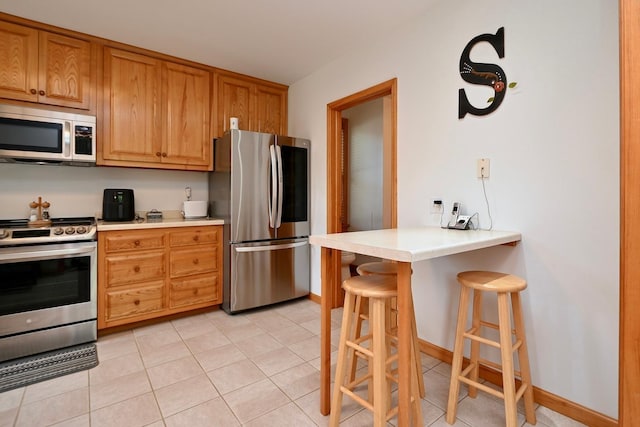 kitchen with a breakfast bar area, light tile patterned floors, brown cabinetry, stainless steel appliances, and light countertops