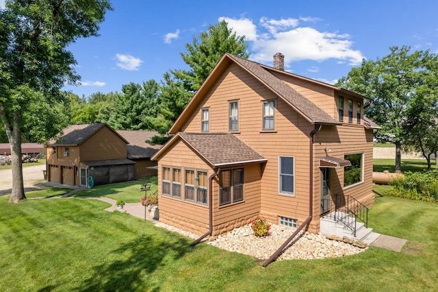 rear view of property featuring a detached garage, a lawn, roof with shingles, and a chimney