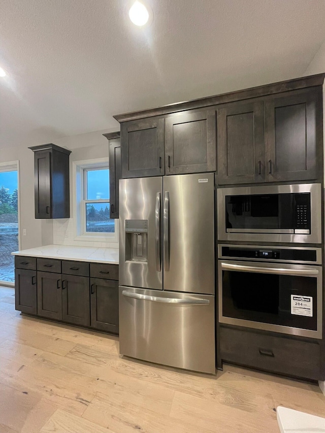 kitchen with tasteful backsplash, stainless steel appliances, a textured ceiling, light countertops, and light wood-type flooring