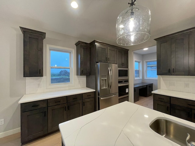 kitchen featuring pendant lighting, stainless steel appliances, tasteful backsplash, light countertops, and dark brown cabinetry