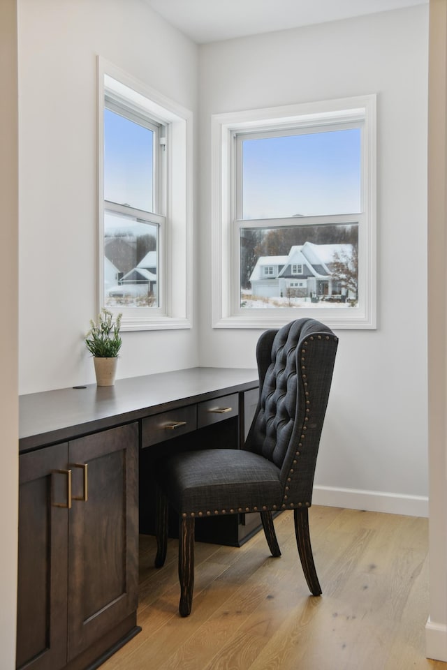 home office featuring light wood-type flooring, built in study area, and baseboards