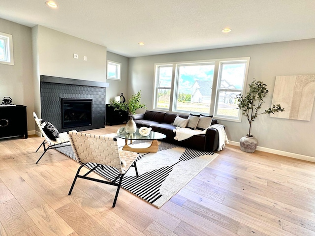 living area with a healthy amount of sunlight, light wood finished floors, a brick fireplace, and baseboards