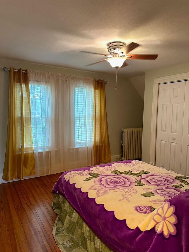 bedroom featuring ceiling fan, wood-type flooring, radiator, and a closet