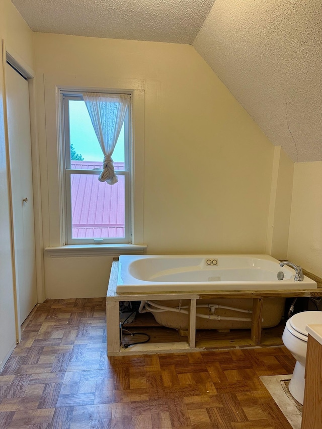 bathroom with a tub, vaulted ceiling, toilet, and a textured ceiling