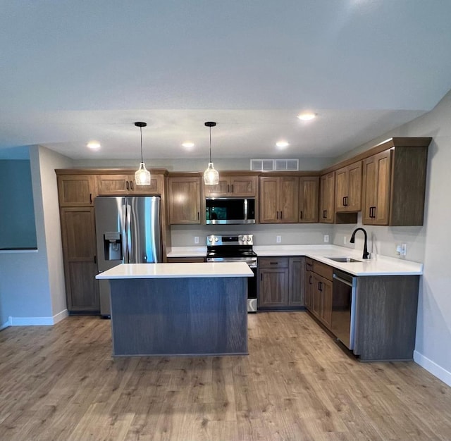 kitchen featuring stainless steel appliances, light wood-type flooring, hanging light fixtures, a center island, and sink