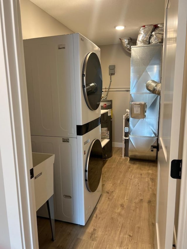 laundry room with heating utilities, stacked washer and dryer, light hardwood / wood-style floors, and water heater