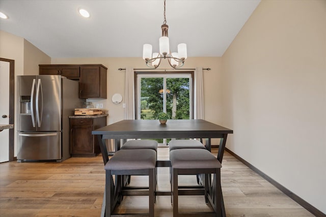 dining space featuring lofted ceiling, light wood-type flooring, and an inviting chandelier