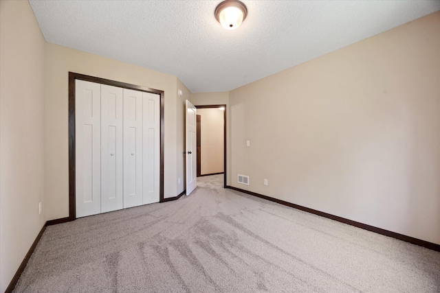 unfurnished bedroom featuring light carpet, a closet, and a textured ceiling