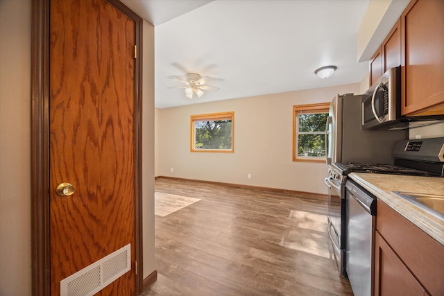 kitchen with appliances with stainless steel finishes, plenty of natural light, ceiling fan, and light hardwood / wood-style flooring