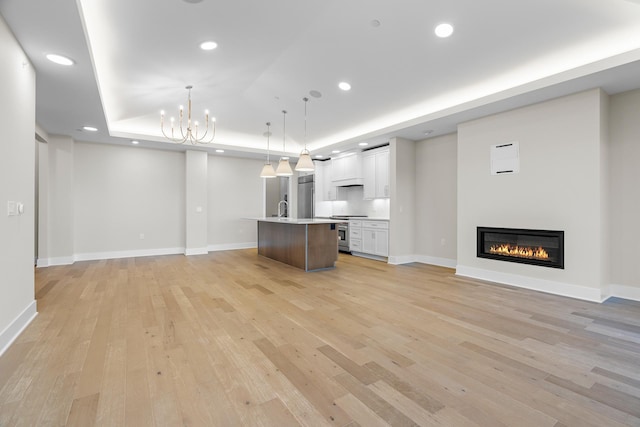 unfurnished living room featuring a tray ceiling, sink, light hardwood / wood-style floors, and an inviting chandelier