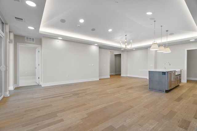 unfurnished living room with a chandelier, light wood-type flooring, a tray ceiling, and sink