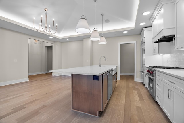 kitchen with white cabinets, premium appliances, a raised ceiling, and a center island with sink