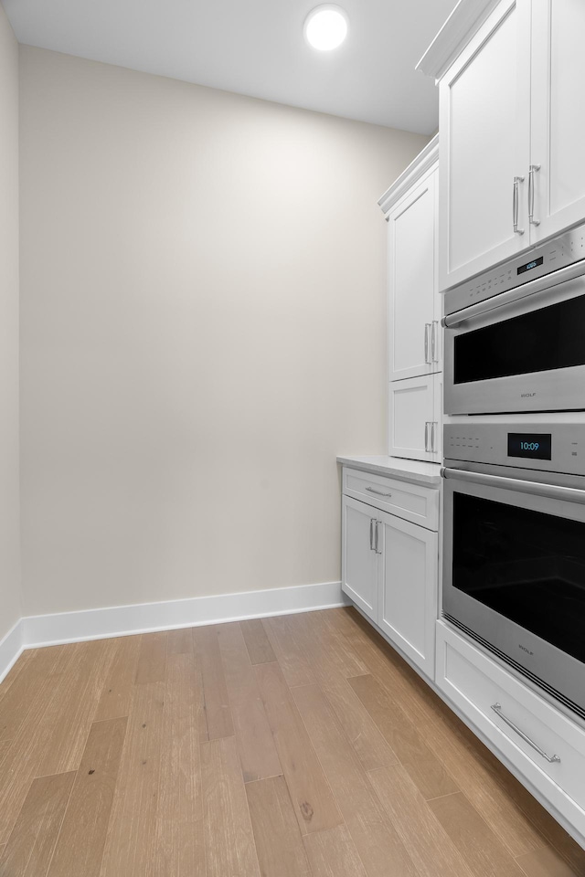 kitchen with white cabinets, stainless steel double oven, and light hardwood / wood-style flooring