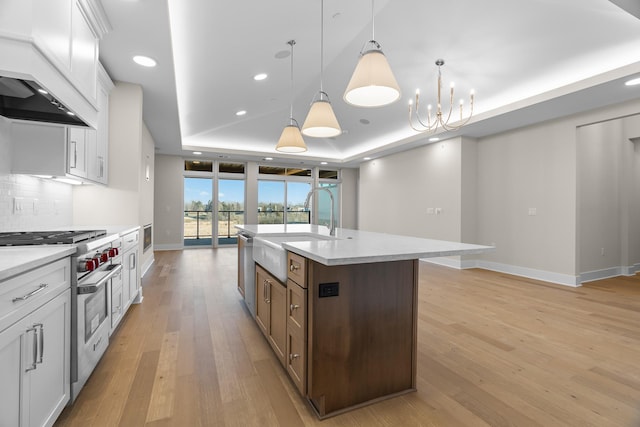 kitchen with decorative light fixtures, white cabinetry, a kitchen island with sink, and a tray ceiling