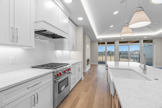 kitchen with white cabinets, premium stove, pendant lighting, and a tray ceiling