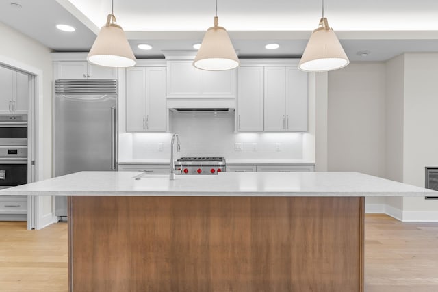 kitchen with white cabinets, hanging light fixtures, stainless steel appliances, and a kitchen island with sink