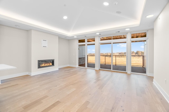 unfurnished living room featuring a raised ceiling and light hardwood / wood-style flooring