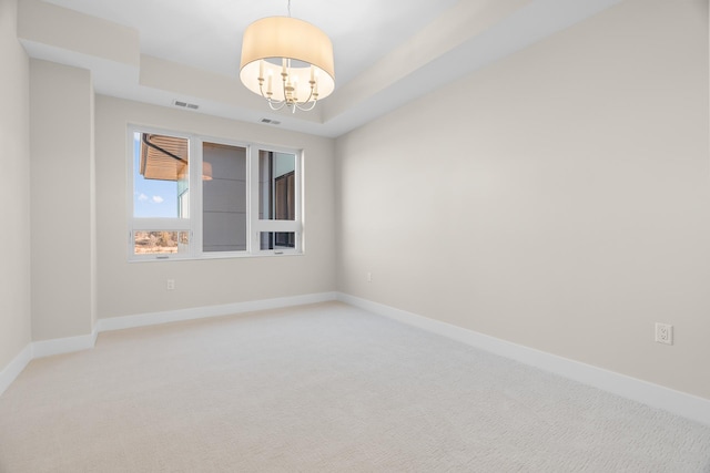 spare room featuring a tray ceiling, carpet, and an inviting chandelier