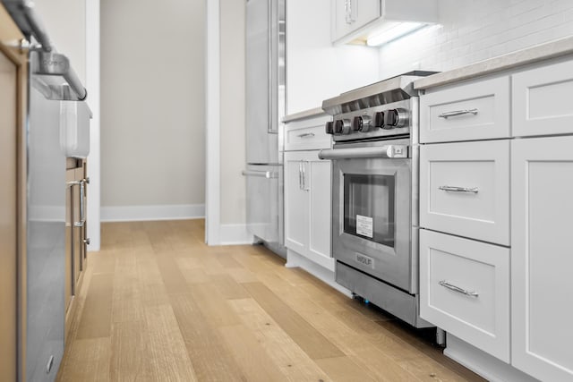 kitchen featuring backsplash, white cabinets, stainless steel appliances, and light wood-type flooring