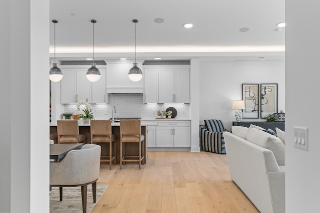 kitchen featuring an island with sink, decorative light fixtures, light wood-type flooring, a kitchen bar, and white cabinetry