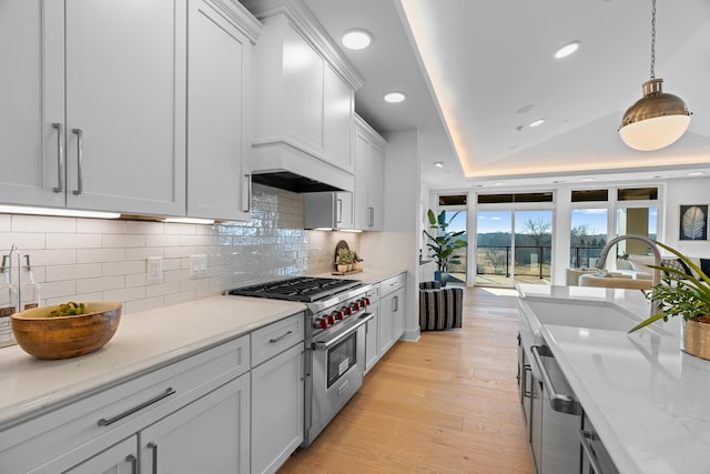 kitchen with luxury stove, a tray ceiling, tasteful backsplash, light wood-type flooring, and pendant lighting