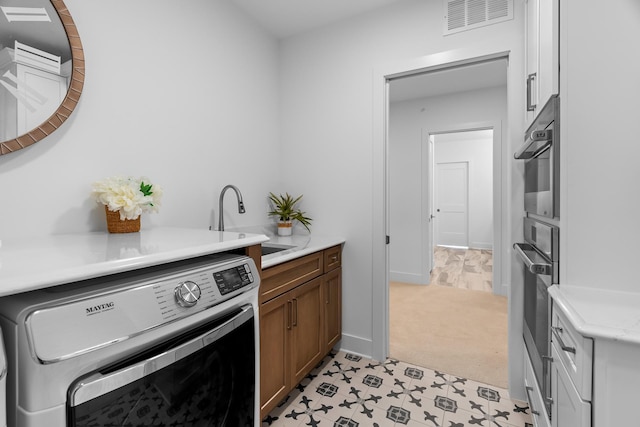 kitchen featuring sink, washer / dryer, and light colored carpet