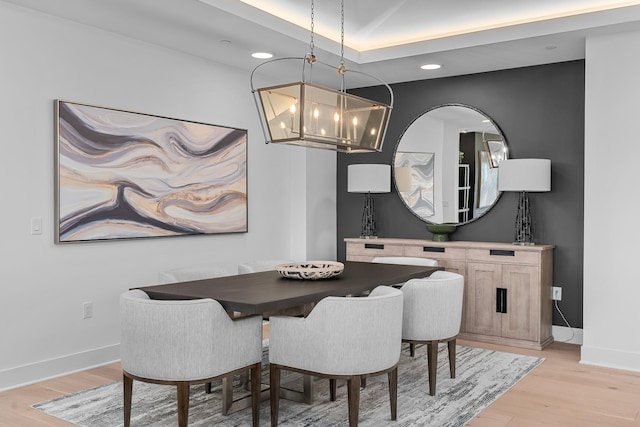 dining area featuring a raised ceiling, light hardwood / wood-style flooring, and an inviting chandelier