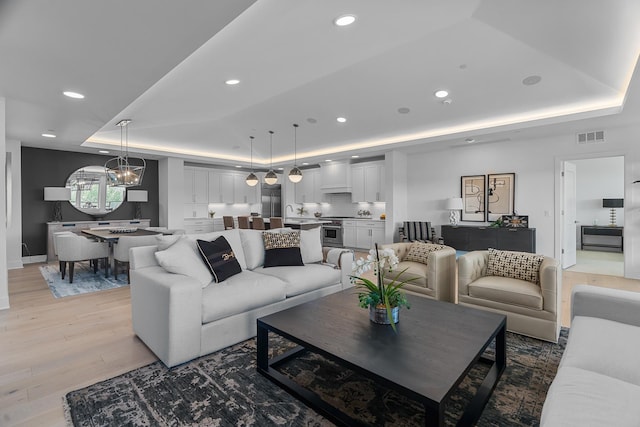 living room with a tray ceiling, sink, wood-type flooring, and an inviting chandelier