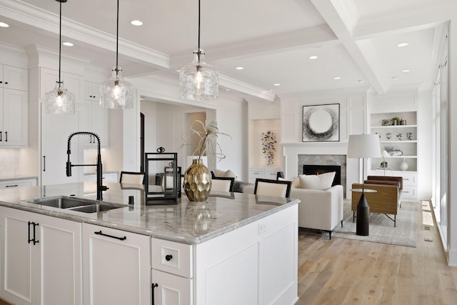 kitchen featuring beamed ceiling, a center island with sink, light wood-type flooring, and white cabinetry